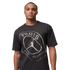 A man wearing a black t-shirt with a metallic silver graphic of the Paris Saint-Germain logo and Jordan Brand Jumpman on a black background.