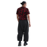 Back view of a man wearing a black t-shirt with a red abstract pattern and baggy black pants against a white background.