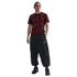 A man in a red and black patterned soccer jersey, baggy black pants, and sneakers, standing against a white background.