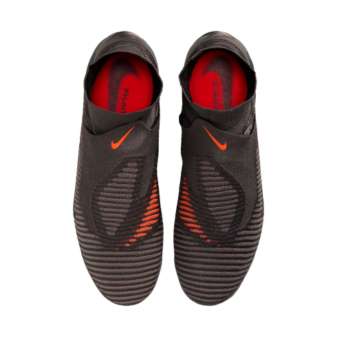 A top-down view of a pair of black Nike Phantom laceless soccer cleats with bright orange accents and a textured upper against a black background.