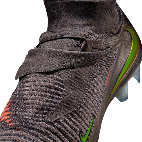 A close-up shot of a dark grey Nike soccer cleat featuring a textured, knitted upper and iridescent green and orange Nike swooshes against a solid black background.