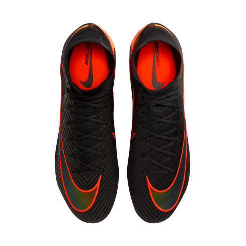 An overhead view of a pair of black Nike Mercurial soccer cleats with vibrant orange accents and black laces, set against a solid black background. The shoes feature large orange swooshes on the forefoot and bright orange interior linings with "MERCURIAL"