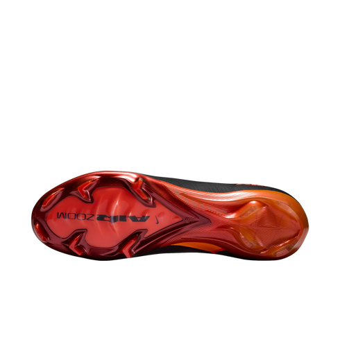 A bottom view of a Nike soccer cleat sole featuring a glossy metallic red and orange gradient against a black background. The forefoot displays chevron-shaped studs and the words "AIR ZOOM" in black.