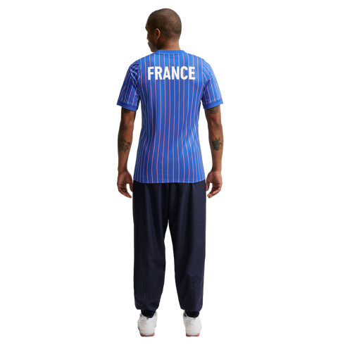 Back view of a person wearing a blue pinstriped "FRANCE" jersey, navy blue joggers, and white sneakers against a white background.