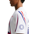 Side profile of a person wearing a white athletic shirt featuring red and blue curved stripes and a circular logo on the sleeve.
