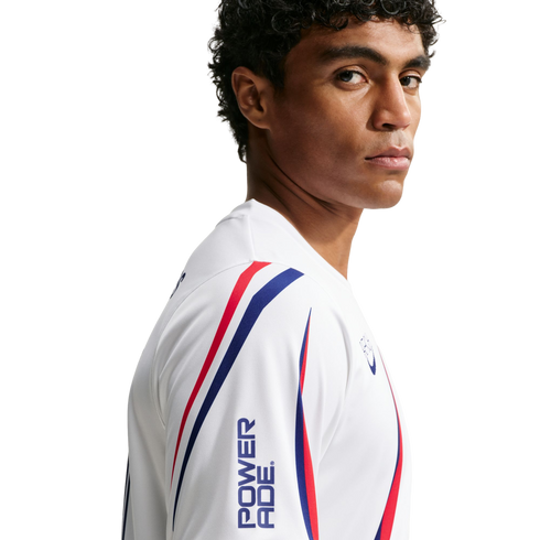 A man with curly hair in a white athletic jersey with red and blue stripes and a Powerade logo, looking over his shoulder against a white background.