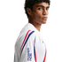 A man with curly hair in a white athletic jersey with red and blue stripes and a Powerade logo, looking over his shoulder against a white background.