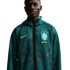 A waist-up portrait of a young Black man wearing a dark teal mesh Nike zip-up hoodie. The hoodie features a yellow Nike swoosh on one side and the Brazil national football team crest with "BRASIL" printed below it on the other. He is looking directly at t