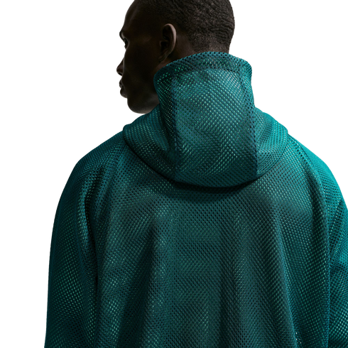 A man is shown from the back, wearing a dark teal hooded garment with a prominent mesh texture. He is looking to his left in profile against a solid black background.
