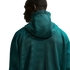 A man is shown from the back, wearing a dark teal hooded garment with a prominent mesh texture. He is looking to his left in profile against a solid black background.