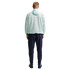 A man stands with his back to the camera, wearing a light mint green mesh hoodie, navy blue pants, and blue sneakers against a black background.