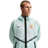 A man wearing a light mint green, mesh Nike zip-up hoodie with the French Football Federation (FFF) crest and black chevron detailing, set against a solid black background.