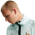 A profile shot of a blond man looking down, wearing a mint green Nike mesh jacket featuring the French National Football Team crest.