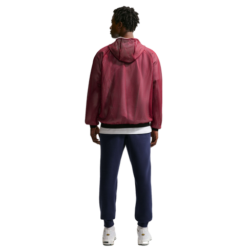 Full-body back view of a man wearing a maroon mesh hooded jacket, navy blue sweatpants, and white sneakers against a black background.