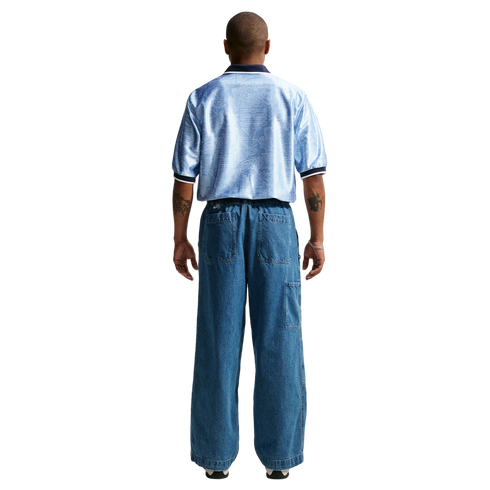 Back view of a man wearing a light blue patterned short-sleeve shirt and wide-leg denim jeans against a white background.