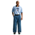 A man models a light blue Nike England jersey tucked into baggy wide-leg blue jeans and black sneakers against a plain white background.