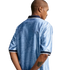 Back view of a man in a patterned light blue polo shirt with navy and white trim, standing against a white background with his hands behind his back.