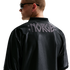 Back view of a man in a black shiny jersey with "NORGE" in grey stylized letters across the shoulders. He wears sunglasses and looks left against a white background.