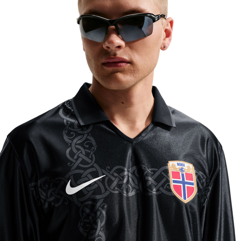 A man in sunglasses wears a black long-sleeved Nike Norway jersey featuring a grey celtic pattern, set against a white background.