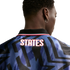 Rear view of a person with short dark hair wearing a blue patterned jersey with "STATES" in white and red text on the back. They are wearing a silver hoop earring.
