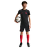 A young boy in a black USA soccer kit and red socks holds a soccer ball against a solid black background.