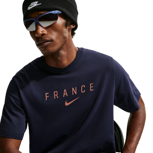 A person wearing a black Nike beanie and blue-framed sunglasses with a navy blue t-shirt featuring "FRANCE" and a rose-gold Nike logo.