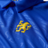 Close-up of a blue textured polo shirt featuring an embroidered yellow lion rampant logo on the chest.
