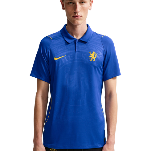 A young man wearing a blue Nike Chelsea FC polo shirt with yellow accents and an embossed club crest, set against a plain white background.