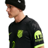 A man in profile wearing a black Nike beanie and a black Atletico Madrid jersey with neon green logos and a Kraken sponsor patch on the sleeve.