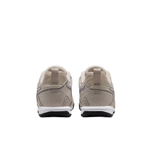 A rear view of a pair of beige sneakers with white midsoles and black outsoles, set against a solid black background.