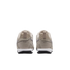 A rear view of a pair of beige sneakers with white midsoles and black outsoles, set against a solid black background.