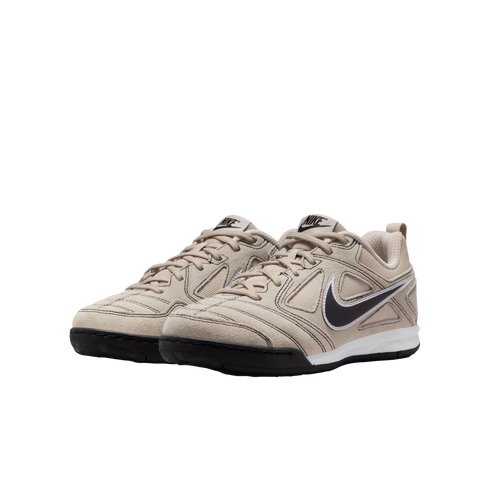 A pair of beige Nike low-top sneakers with black swooshes and soles, set against a solid black background.