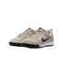 A pair of beige Nike low-top sneakers with black swooshes and soles, set against a solid black background.