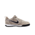 Side view of a tan Nike athletic sneaker featuring a black swoosh, white midsole, and black outsole against a solid black background.