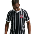 A person with braided hair looks down, wearing a black and white vertically striped Nike soccer jersey with a red and white crest. The background is solid black.
