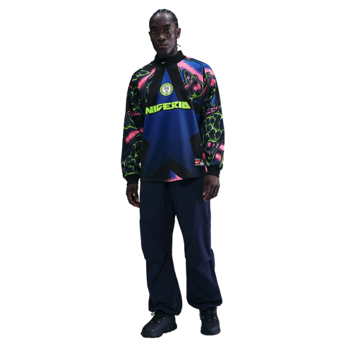 A man models a long-sleeve Nike Nigeria soccer top with a colorful abstract pattern on the sleeves and navy pants against a solid black background.