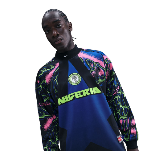 A person wearing a vibrant Nike Nigeria soccer jersey with pink, blue, and lime green patterns against a black background.