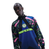 A person wearing a vibrant Nike Nigeria soccer jersey with pink, blue, and lime green patterns against a black background.