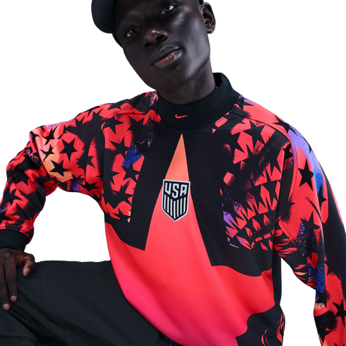 A person wearing a Nike USA soccer long-sleeve shirt featuring a bold red and black star pattern and the USA crest, set against a black background.