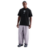 A man stands against a black background wearing a black Nike T-shirt with a USA crest and loose grey pants.
