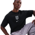A man wearing a black Nike USA soccer T-shirt and grey cargo pants poses against a black background.