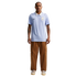 Full-body portrait of a man wearing a light blue Uruguay national team soccer jersey with a white collar, paired with brown cargo pants and beige sneakers against a solid black background.