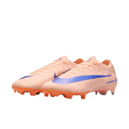 Peach-colored Nike soccer cleats with a large iridescent blue swoosh and orange studs, set against a black background.