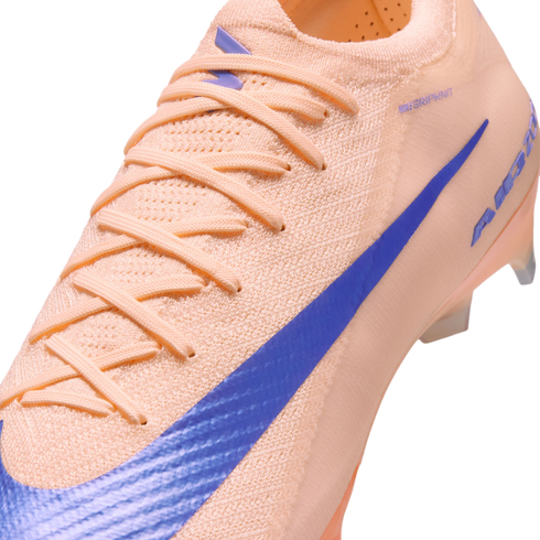 Close-up of a peach-colored Nike soccer cleat with a blue swoosh and a textured knit upper.