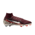 A side profile of a Nike Mercurial soccer cleat against a solid black background. The shoe features a textured burgundy knit upper with a high-top collar, a large metallic silver swoosh, and a heel wrapped in a bold black, red, and cream camouflage-like p