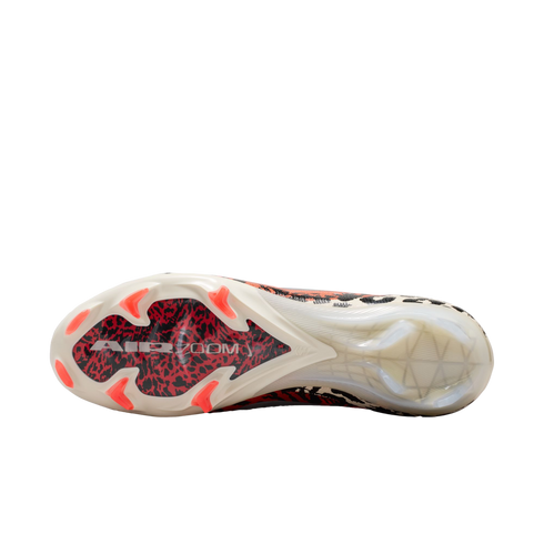 A bottom-up view of a soccer cleat against a black background, showcasing a white sole with a red and black graphic under the forefoot labeled "AIR ZOOM." The shoe features bright orange studs and a translucent heel section.