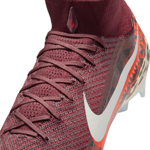 A close-up, high-angle shot shows a maroon Nike soccer cleat against a black background. The shoe features a textured, knit upper with maroon laces and a high-top sock collar. A small, teardrop-shaped logo with a red swoosh is on the front of the collar,