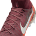 A close-up, high-angle shot shows a maroon Nike soccer cleat against a black background. The shoe features a textured, knit upper with maroon laces and a high-top sock collar. A small, teardrop-shaped logo with a red swoosh is on the front of the collar,