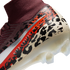 A close-up, angled view of the heel and ankle area of a Nike soccer cleat against a black background. The shoe features a burgundy ribbed knit ankle collar and a main body decorated with a bold leopard-print pattern in cream, black, and vibrant orange. A
