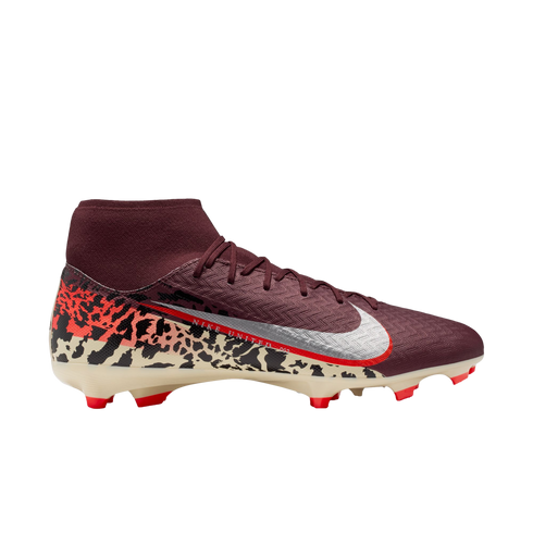 A profile view of a maroon Nike Mercurial soccer cleat against a black background. The shoe features a sock-like ankle collar, silver Swoosh with a red outline, and a cream-colored soleplate with orange studs. A bold graphic pattern in black, orange, and